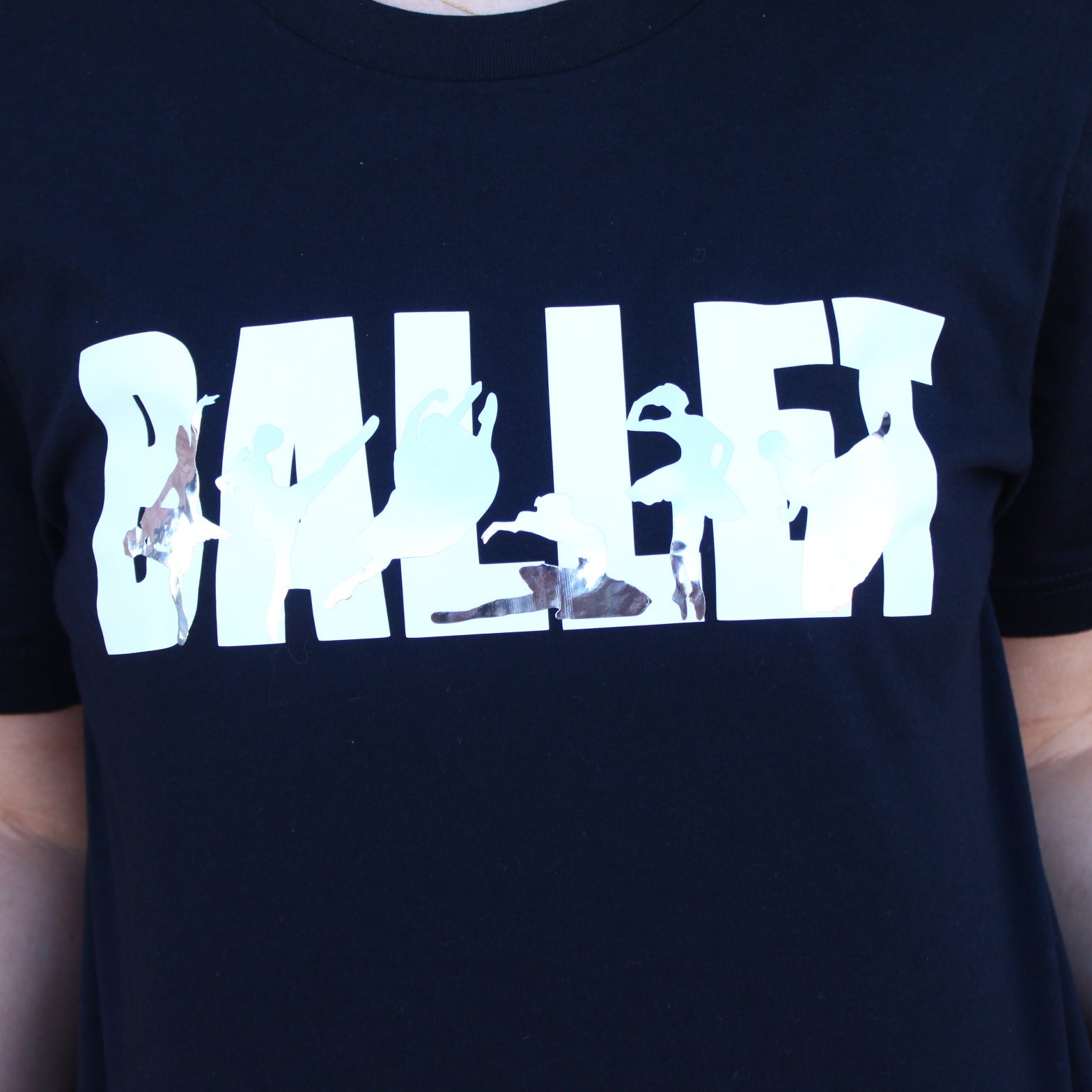 Ballet in white block letters on black t shirt with iconic ballet variations in silver silhouettes. La Esmeralda, Cupid and Kitri from Don Quixote, Dying Swan or Odette from Swan Lake, Raymonda, and Giselle Act 2.